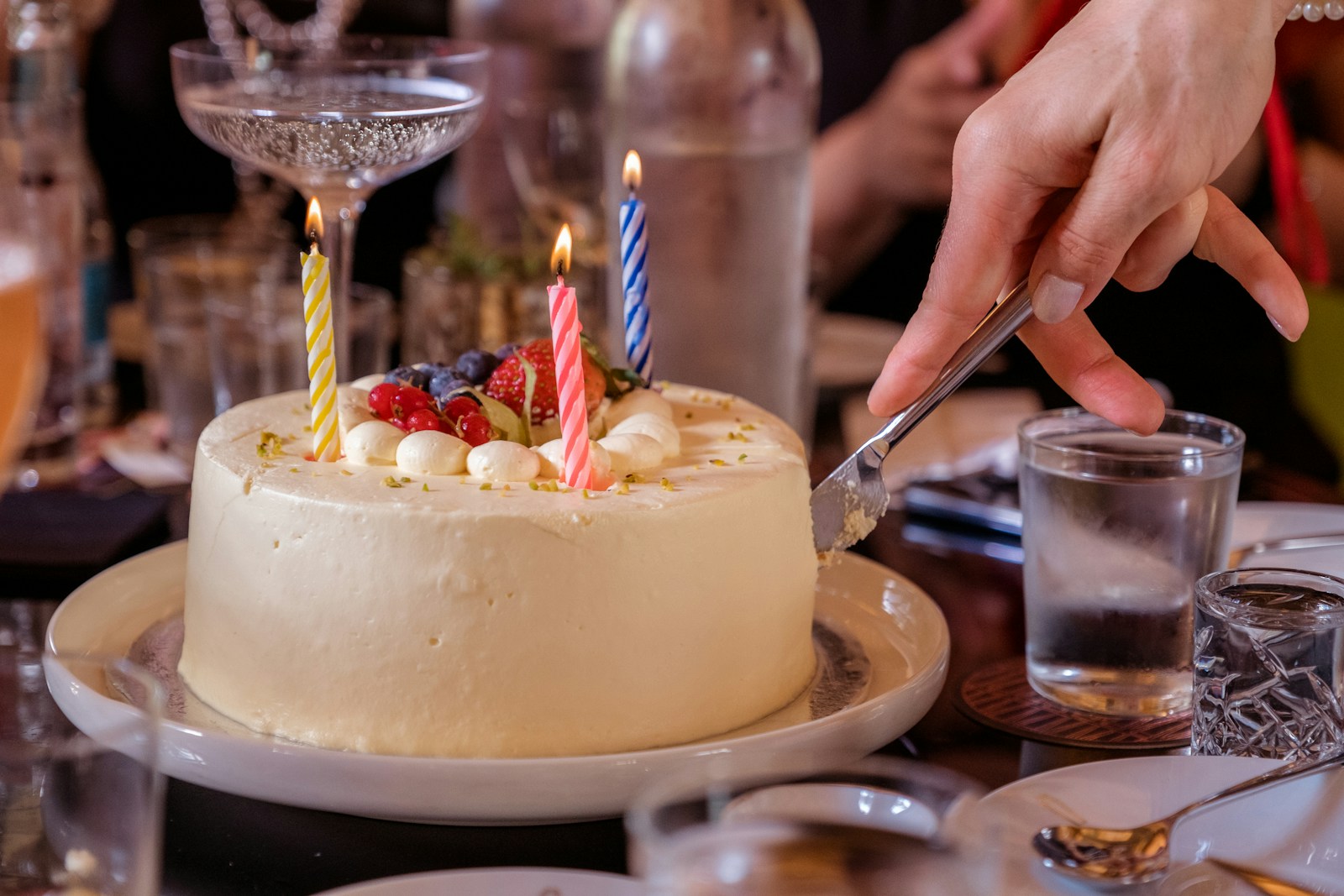 A birthday cake being cut, candles still lit on top