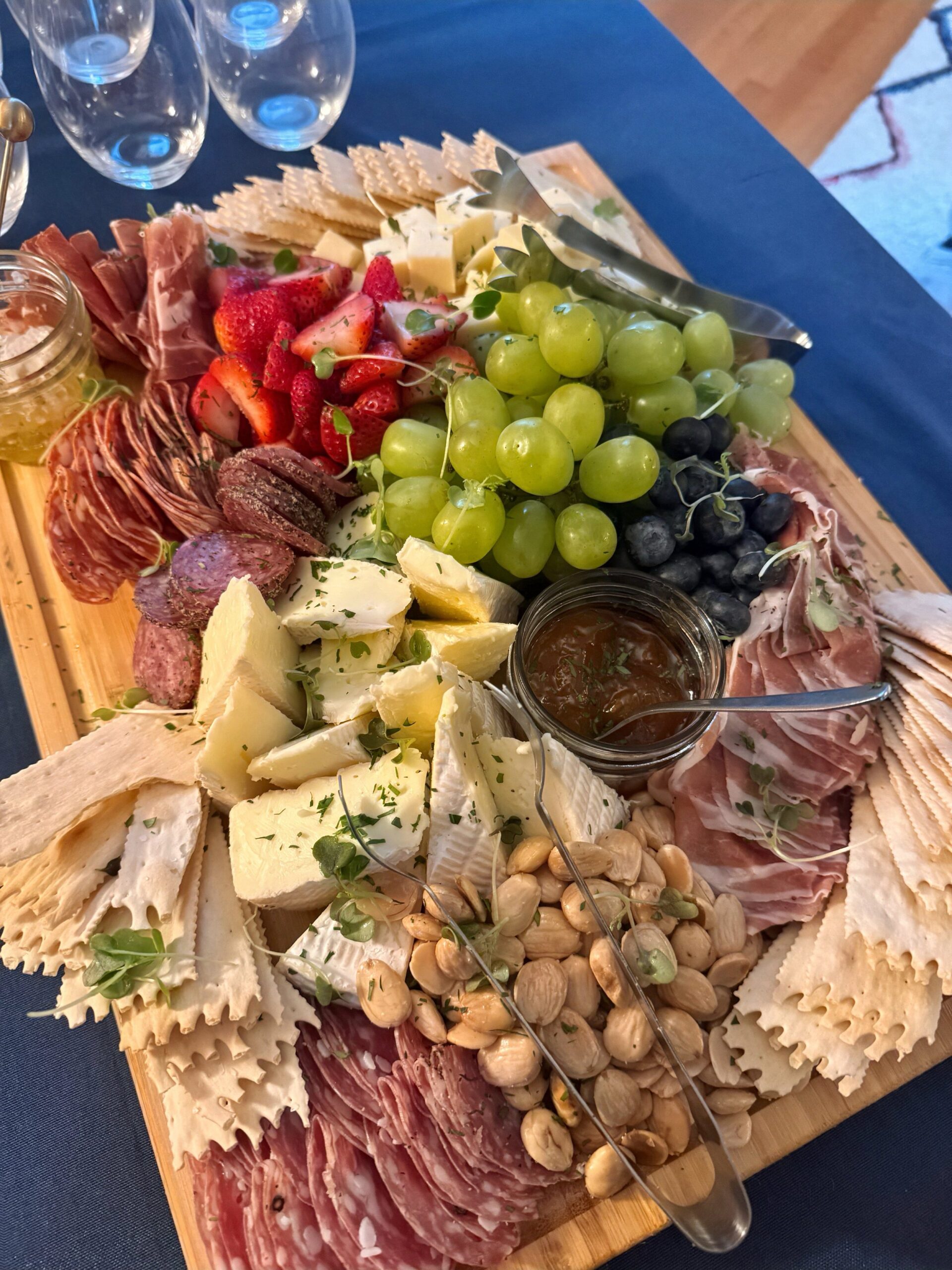Charcuterie board with grapes, strawberries, assorted cheeses, meats, nuts, crackers, and a jar of jam.