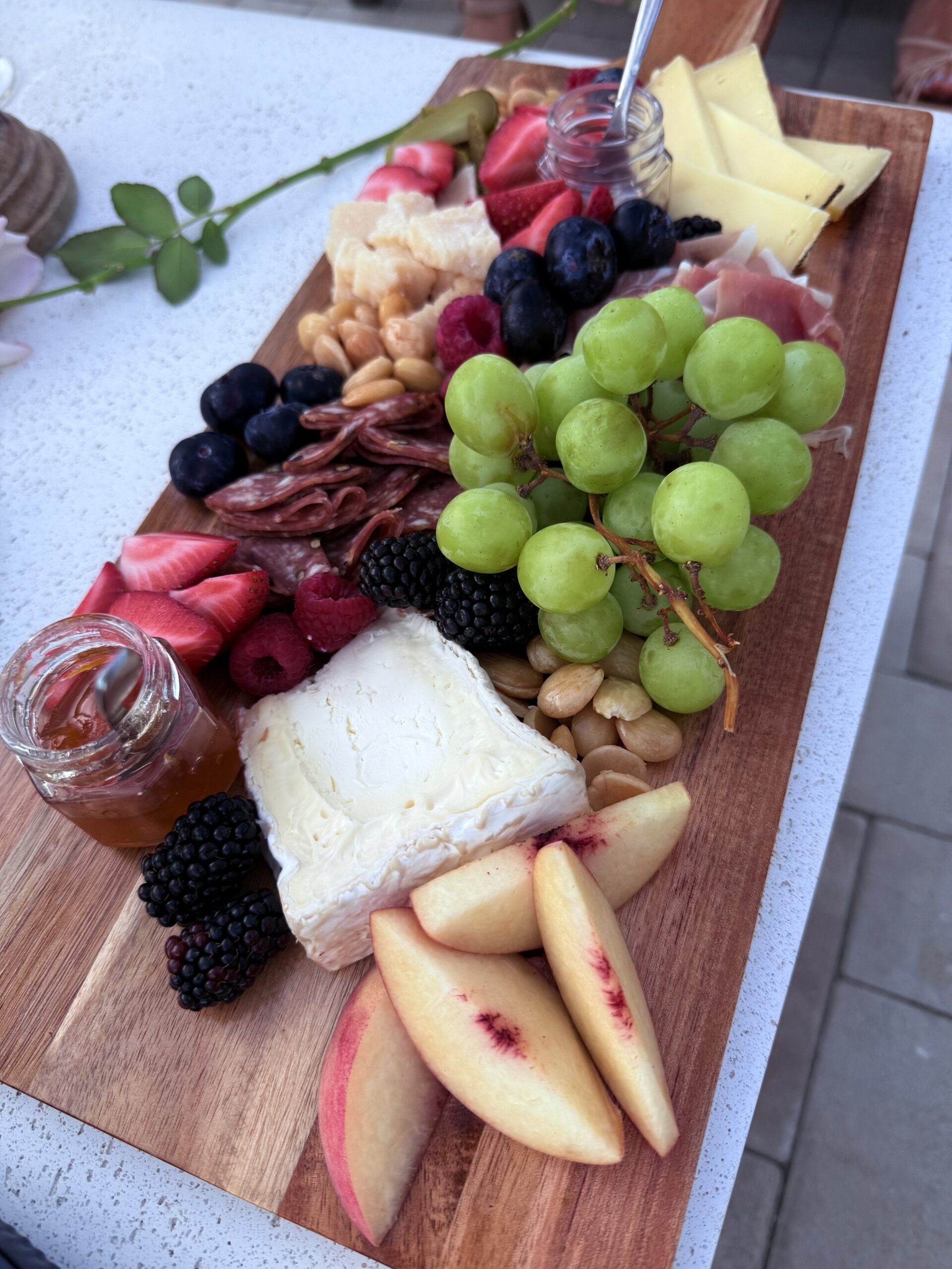 Charcuterie board with grapes, cheese, sliced apples, berries, nuts, sliced meats, and small jars of honey.